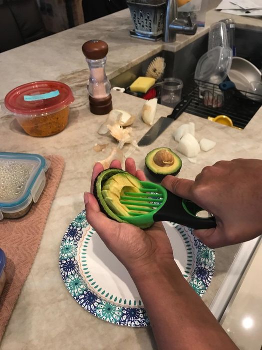 a reviewer’s photo of a hand using the 3-in-1 tool to slice an avocado into multiple pieces