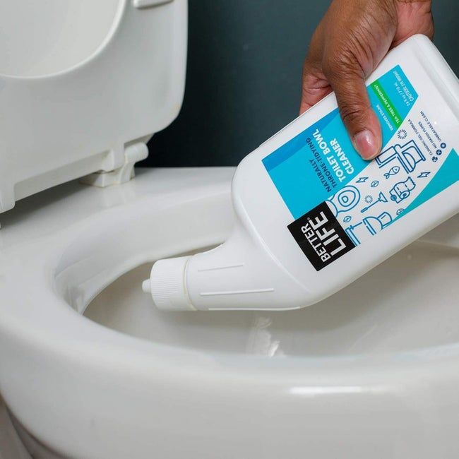 A hand dispenses cleaner from a bottle, with the neck angled to easily reach under the toilet rim.