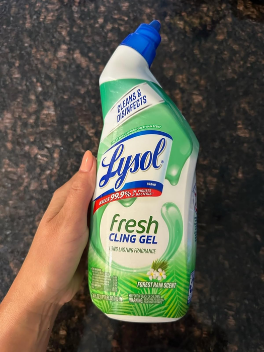 A person holding a bottle of Lysol Fresh Cling Gel cleaner, promising a long-lasting fragrance and advertised to eliminate 99.9% of viruses and bacteria.