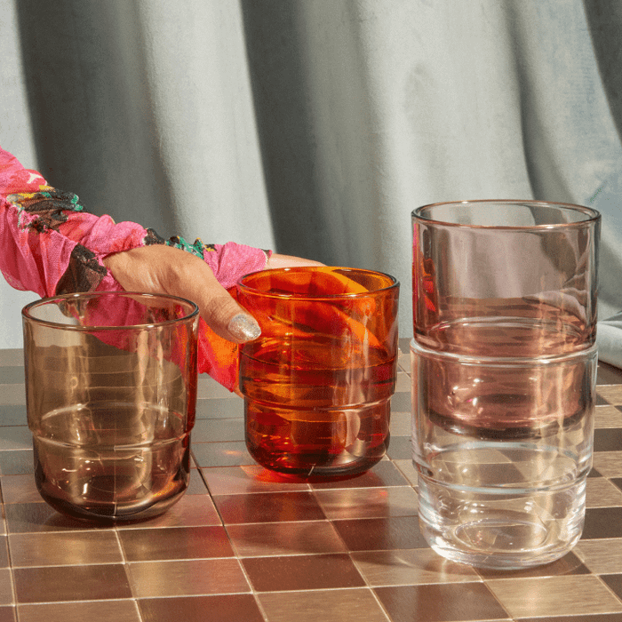 A model picking up an orange glass from a table filled with various drinking glasses