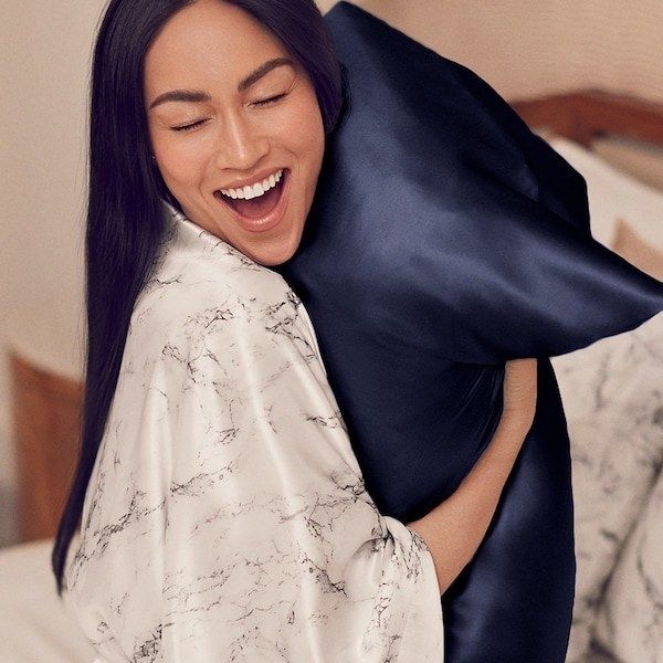 a model embracing a pillow adorned with a navy Slip silk pillowcase