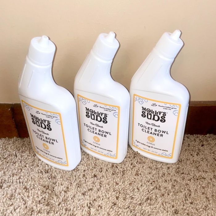 Three bottles of Molly's Suds toilet bowl cleaner standing on a carpet, placed next to a baseboard.