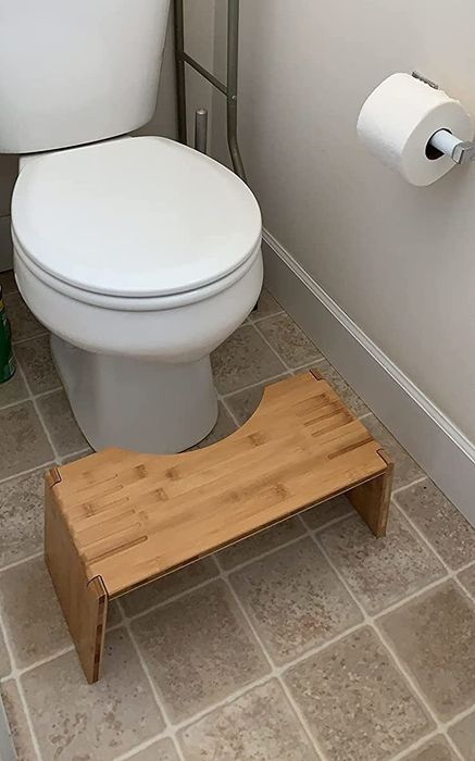 A reviewer’s photo of the bamboo Squatty Potty placed in front of a toilet, showing off its light wood design.