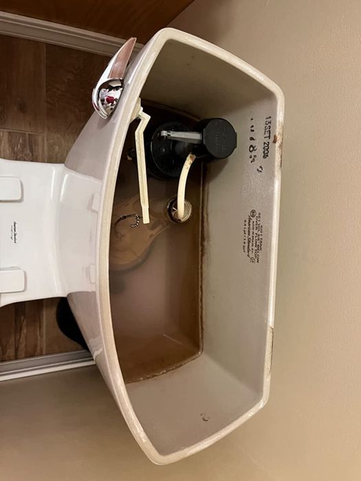 A before shot of a toilet tank with brown stains visible along the sides.
