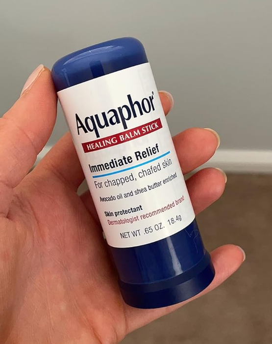 A hand holding a blue Aquaphor Healing Balm Stick labeled