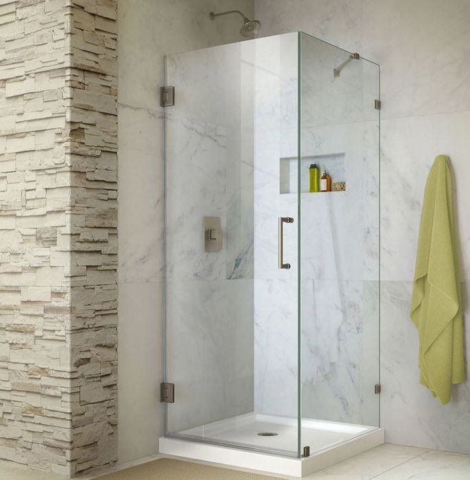 A sleek glass shower enclosure with a hanging towel and a decorative rock wall in the corner