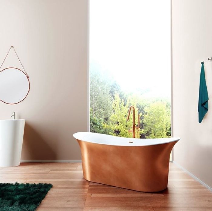A copper freestanding bathtub placed by the window with a green rug