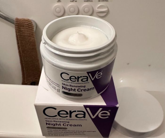 The CeraVe Skin Renewing Night Cream jar sits open, placed on top of its packaging on a bathroom counter.