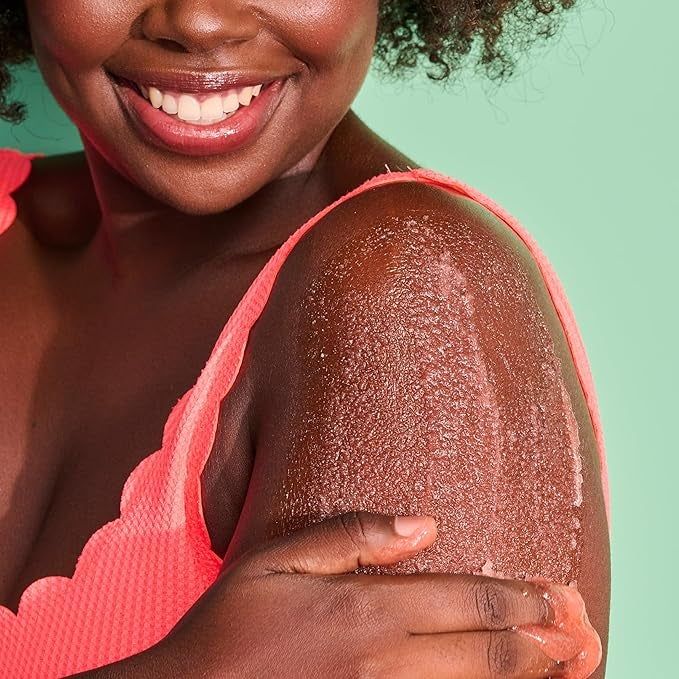 A person grinning while applying exfoliating scrub to their arm, showcasing their skincare regimen