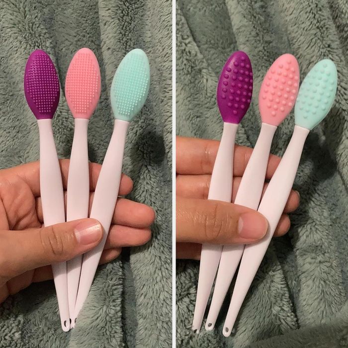 A close-up shot of hands holding silicone exfoliating brushes with textured heads, arranged neatly on a soft fabric backdrop.