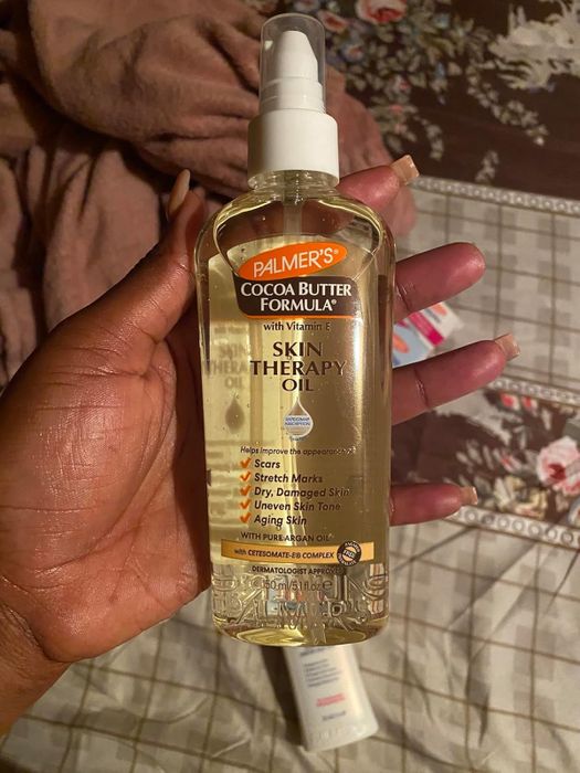 A person holding a bottle of Palmer's Cocoa Butter Formula Skin Therapy Oil, claiming to improve scars, stretch marks, and uneven skin tone.