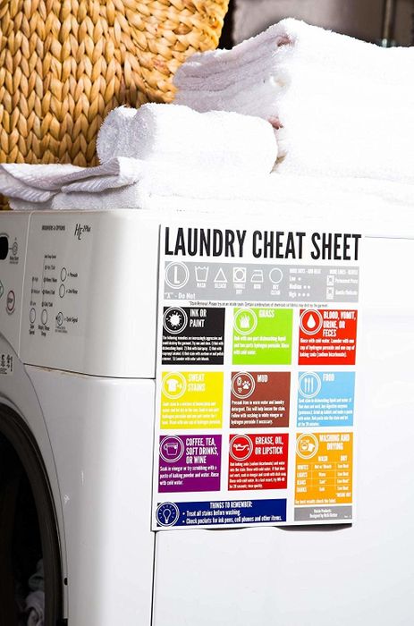 Laundry machine with a Laundry Cheat Sheet on stain removal stuck to the front, and a neatly folded pile of white towels on top