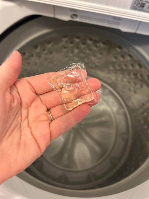 A person is holding a laundry detergent pod in front of an open washing machine.
