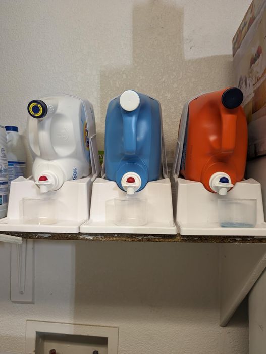Three large detergent containers placed on dispensers, lined up neatly on a shelf in a laundry room.