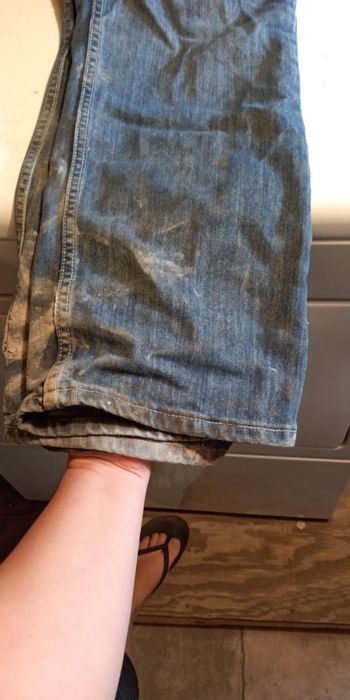 A person's hand lifting a pair of dirty jeans, folded to reveal the inside of the pant leg.