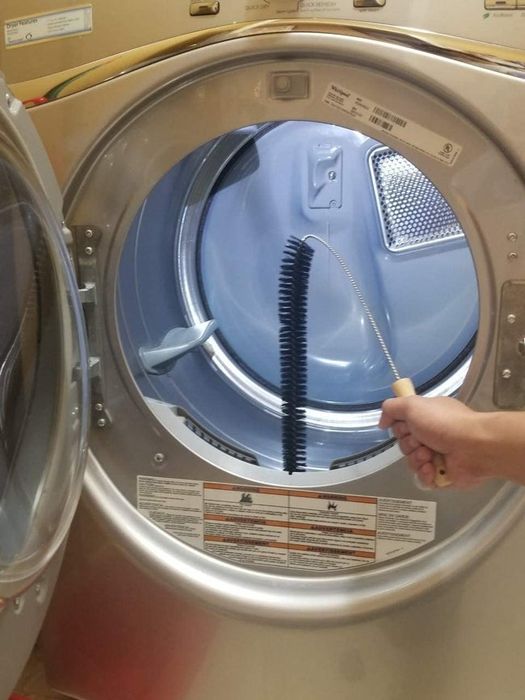 A person using a long brush to clean out the lint trap in a front-load clothes dryer