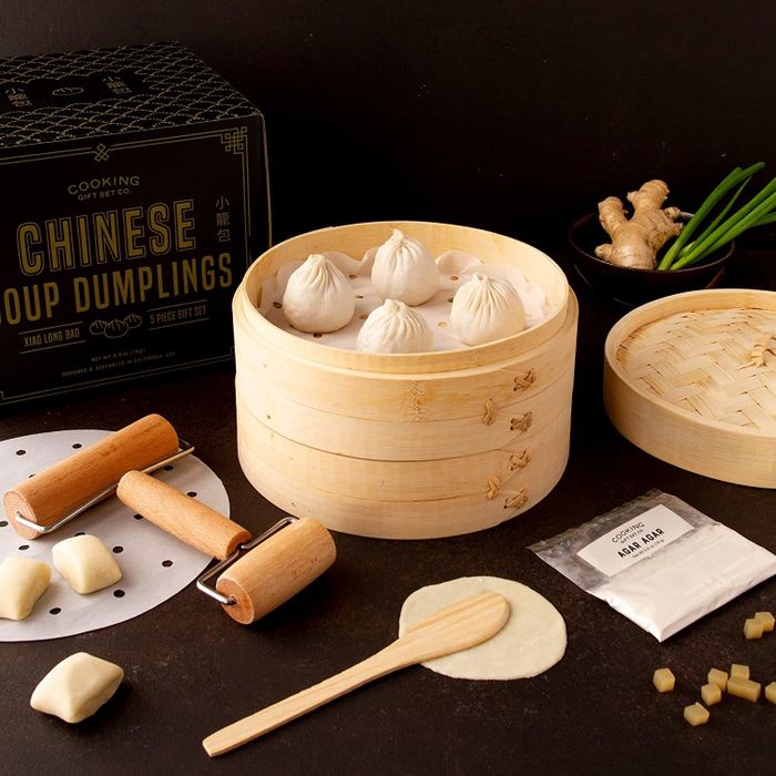 Soup dumplings arranged in a wooden basket with tools and dough scattered around them.