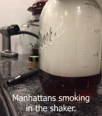 A reviewer’s photo showing a jar filled with smoke and the product behind it, labeled 'Manhattans smoking in the shaker.'