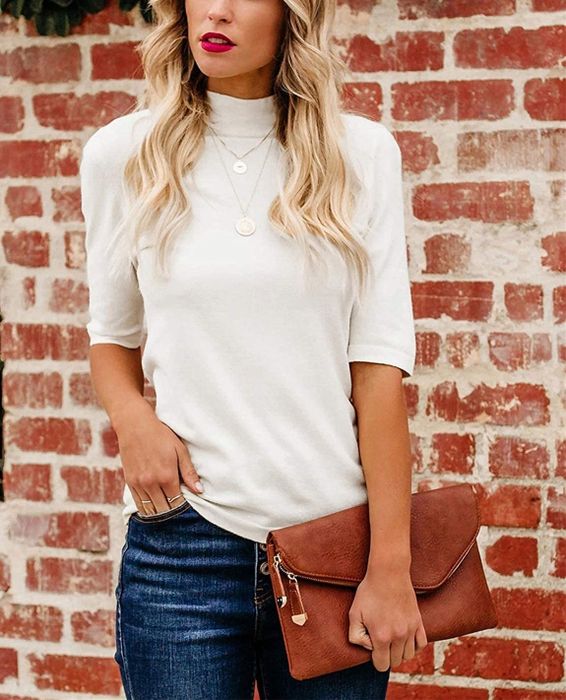 The model is wearing a white turtleneck with jeans, holding a leather clutch