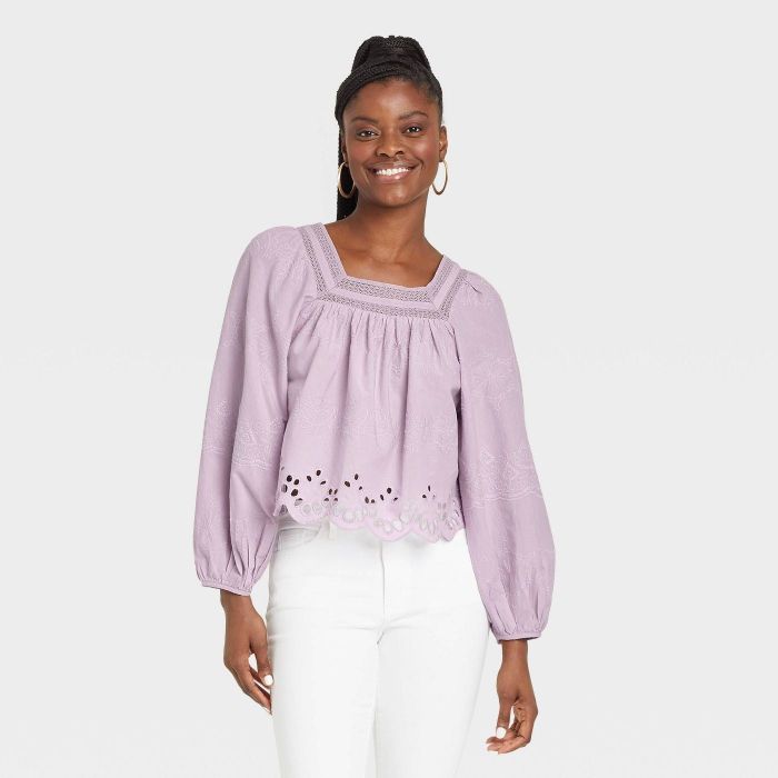 The model is wearing the top in purple, paired with white pants