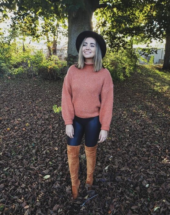 A reviewer shares a photo of herself in a pink sweater paired with leggings and thigh-high boots.