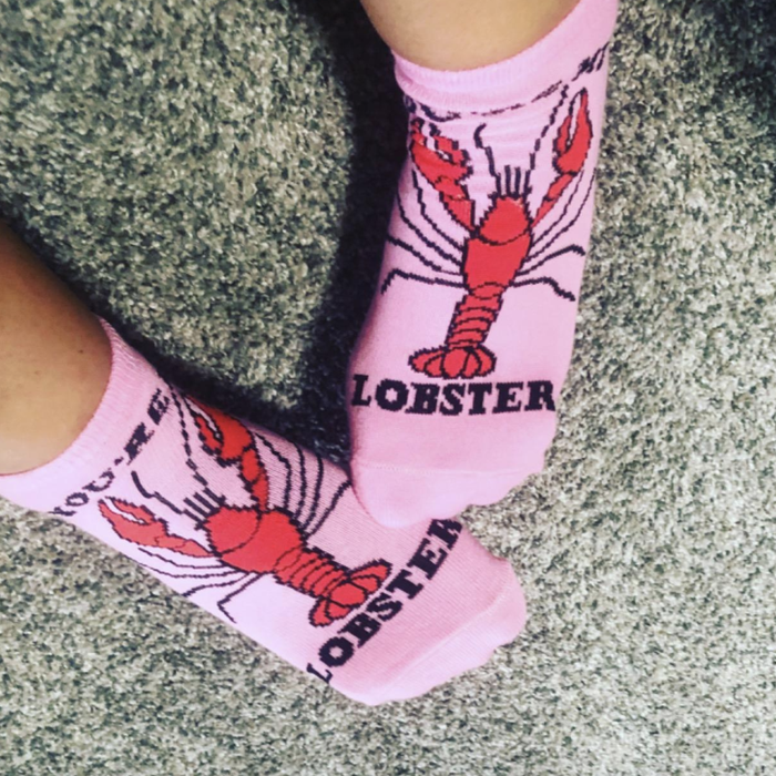 A reviewer showing off pink socks decorated with a red lobster pattern.