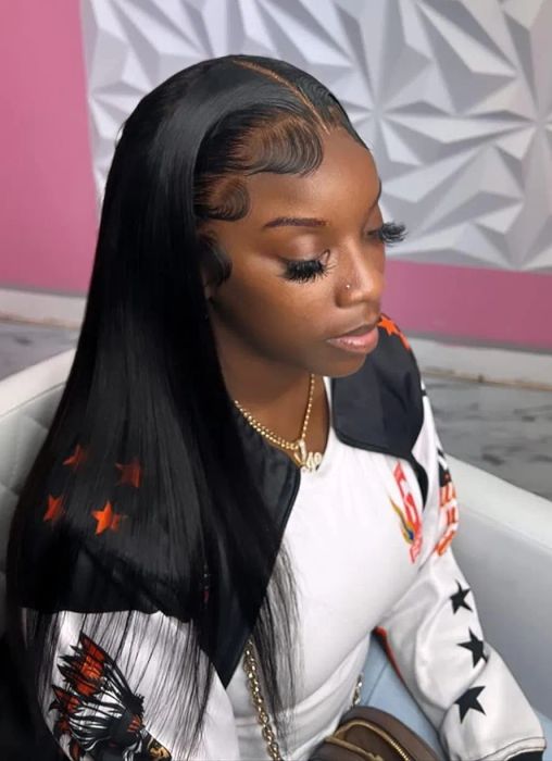 A person with sleek, long hair and flawless makeup is wearing a chic jacket featuring star patterns and a chain necklace, sitting comfortably indoors.
