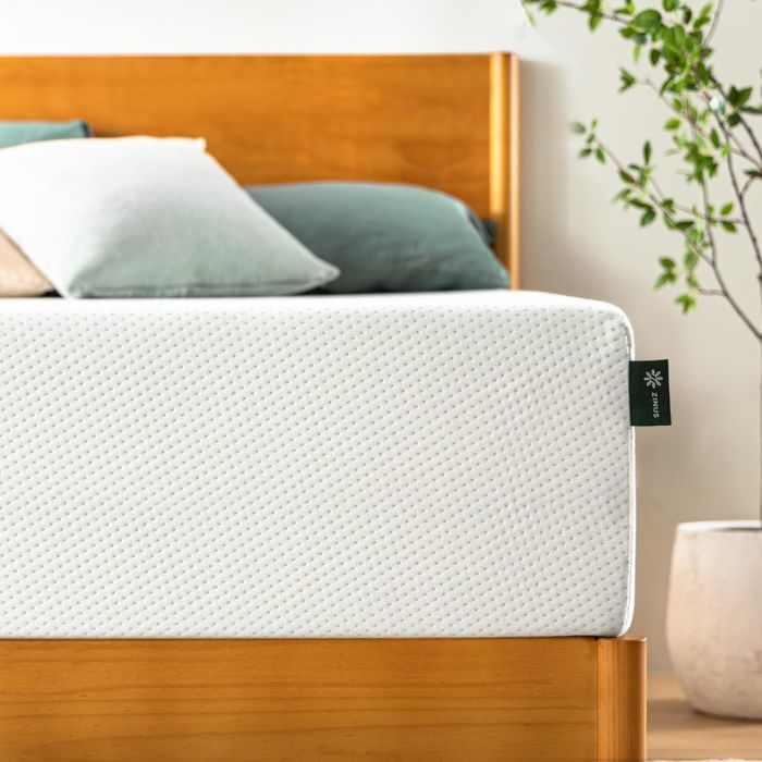A mattress with a visible tag, placed on a wooden bed frame next to a white potted plant for a minimalist and fresh look.