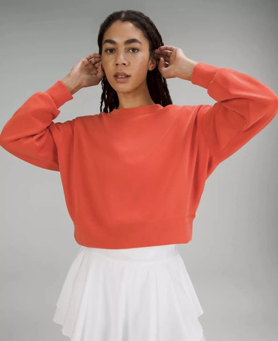 Model with arms raised, wearing an orange sweatshirt and paired with a white tennis skirt