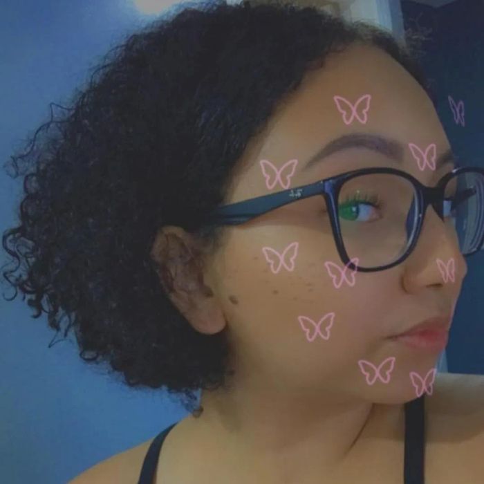 A person with curly hair and glasses is wearing pink butterfly filters on their face.
