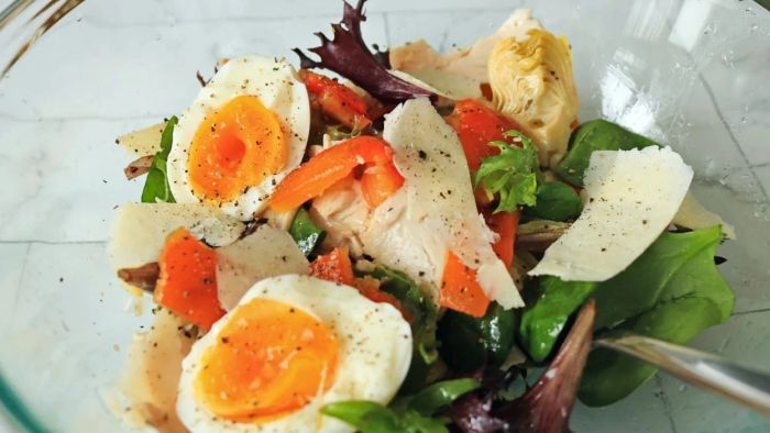 A sandwich salad with ingredients like boiled eggs, shaved cheese, roasted red peppers, and artichoke hearts.