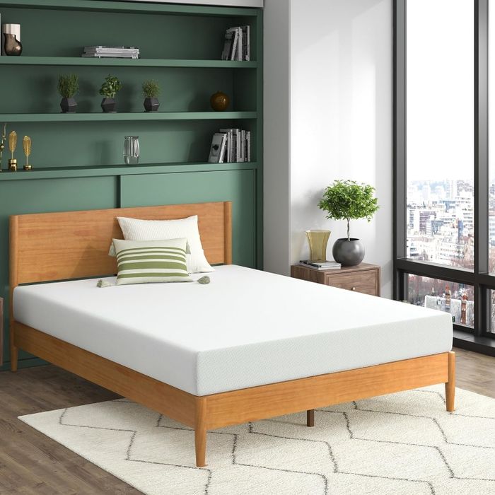 A modern bedroom featuring a minimalist bed design with a wooden headboard, accent pillows, and a neatly arranged mattress that enhances the overall clean and stylish aesthetic.