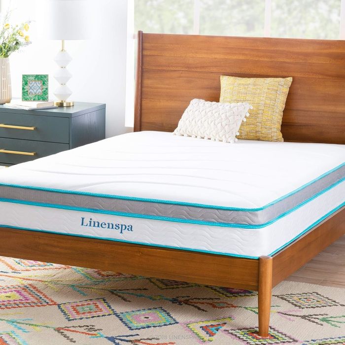 A Linenspa mattress rests on a wooden bed frame, styled with an assortment of pillows, all in a beautifully arranged bedroom.