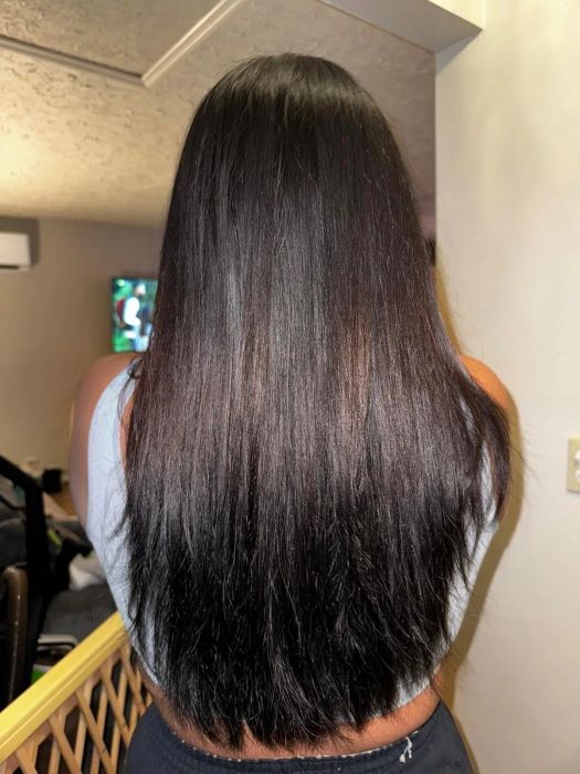 A person with long, straight, dark hair seen from the back in a casual indoor environment.