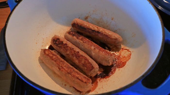 Four sausages sizzling away in a Dutch oven.