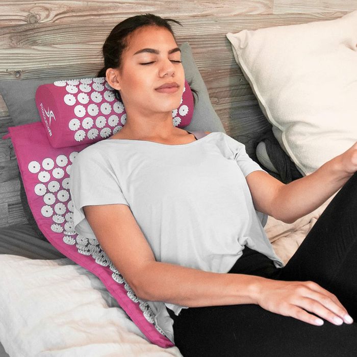 A model relaxing on a pink and white acupressure mat and pillow.