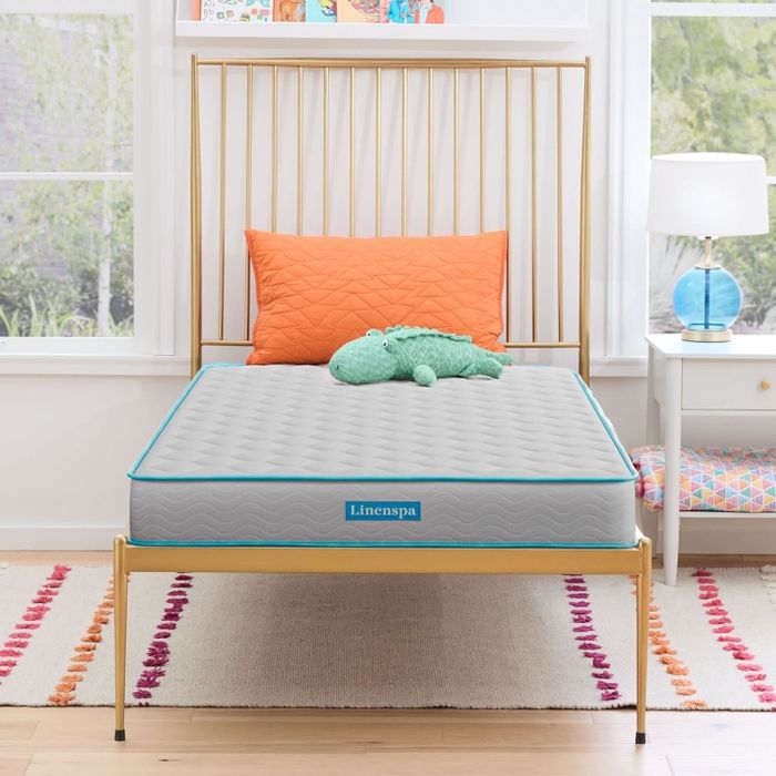 A mattress with a bedspread and plush toy on it, set up in a cozy bedroom for a shopping article.