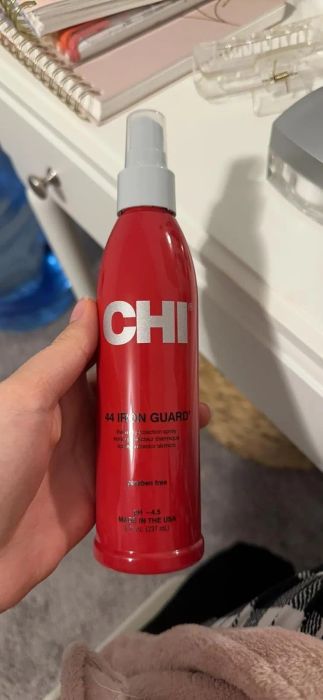 A hand is holding a bottle of CHI 44 Iron Guard thermal protection spray, designed to protect hair from heat damage while styling.