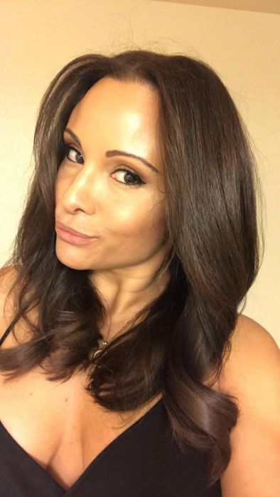 A woman with long, wavy hair takes a close-up selfie while wearing a black top.