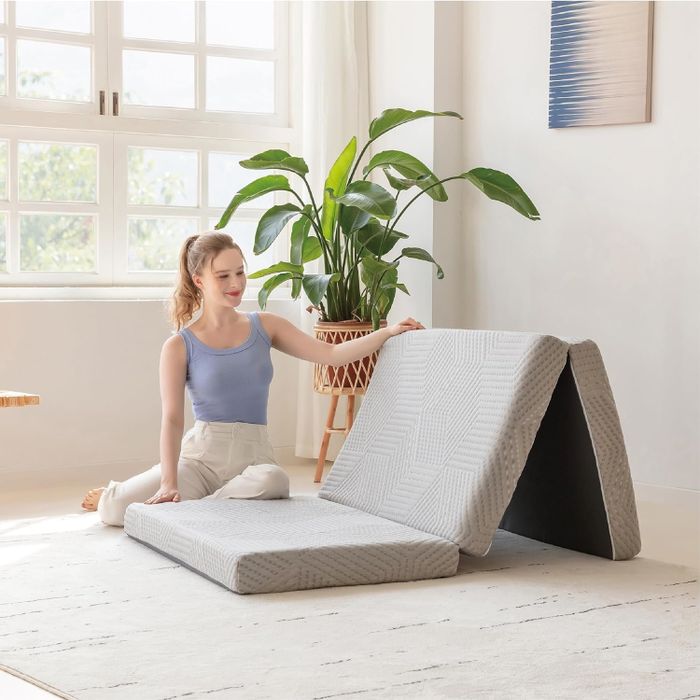 A woman is sitting beside an open, foldable mattress, which is perfect for compact living environments where space-saving is essential.