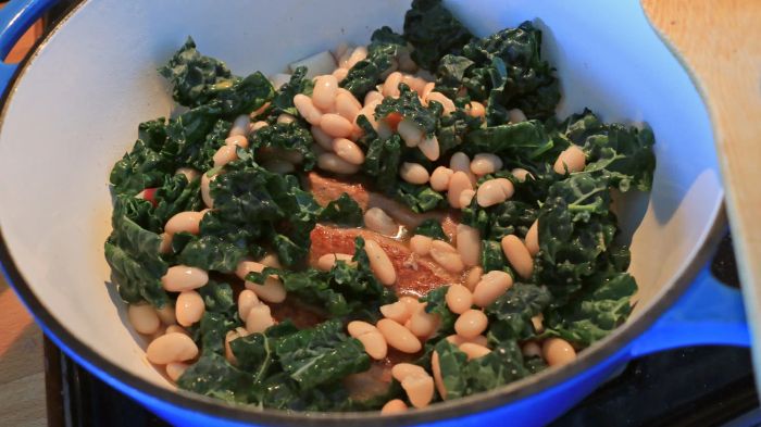 Kale, beans, sausage, and potatoes all simmering together in a Dutch oven pot.