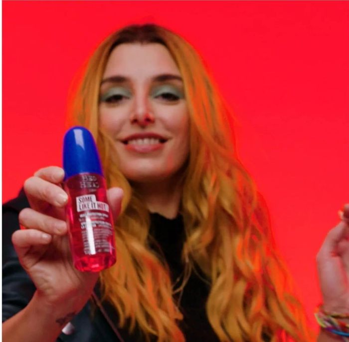 A person is holding a bottle of Tresemmé hair product and smiling towards the camera, set against a neutral background.