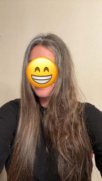 A person with long, wavy hair, dressed in a black top, with a smiling emoji covering their face.