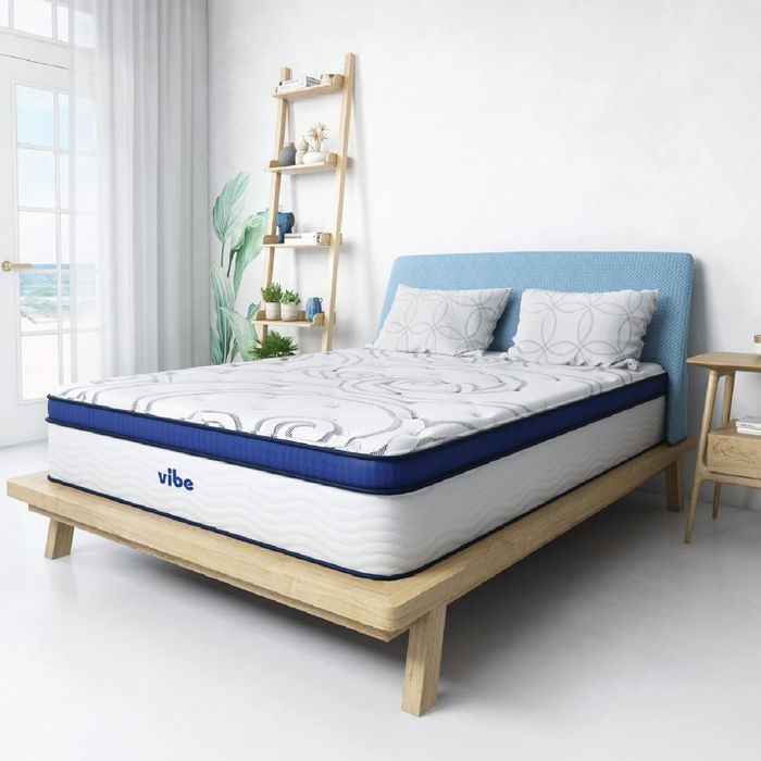 A Vibe-branded mattress resting on a simple wooden bed frame in a bright, modern bedroom, creating a minimalist and inviting atmosphere.