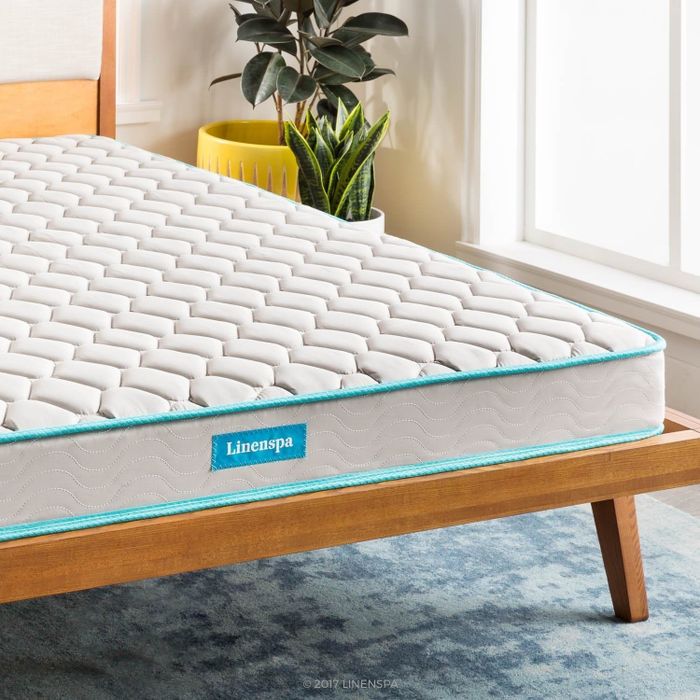 A Linenspa mattress resting on a wooden bed frame, complemented by a potted plant for a natural, serene touch.