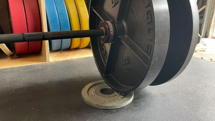 a small weight resting on the ground, slightly elevating one end of a barbell with plates