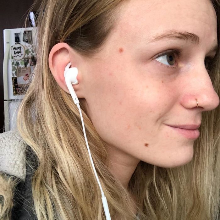 A reviewer wearing Apple Ear Buds with the hooks attached, keeping them firmly in place.