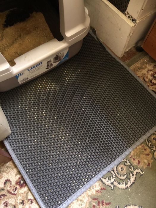 A reviewer’s photo shows the litter trapper mat placed under their litter box on a carpeted floor, with litter visibly caught in the honeycomb design.