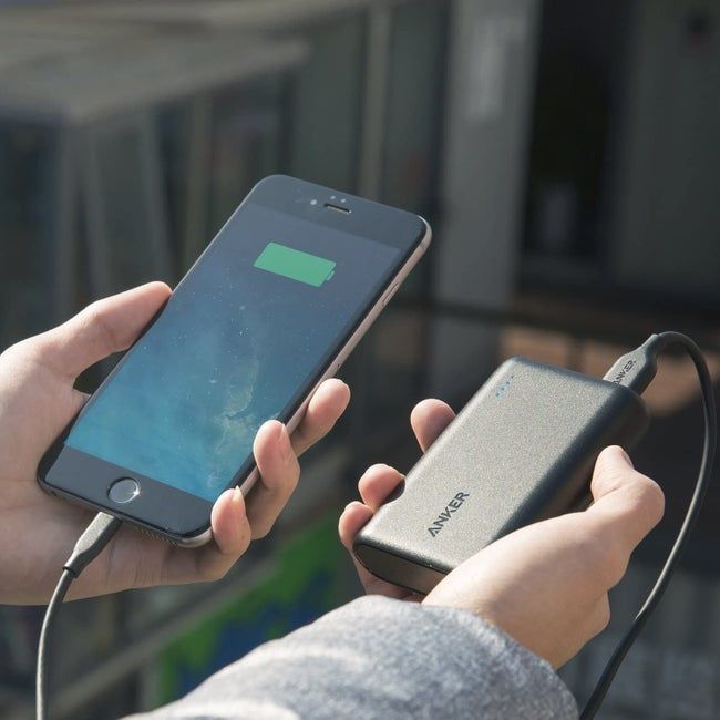 A model holding a small, rectangular black power bank attached to a phone.