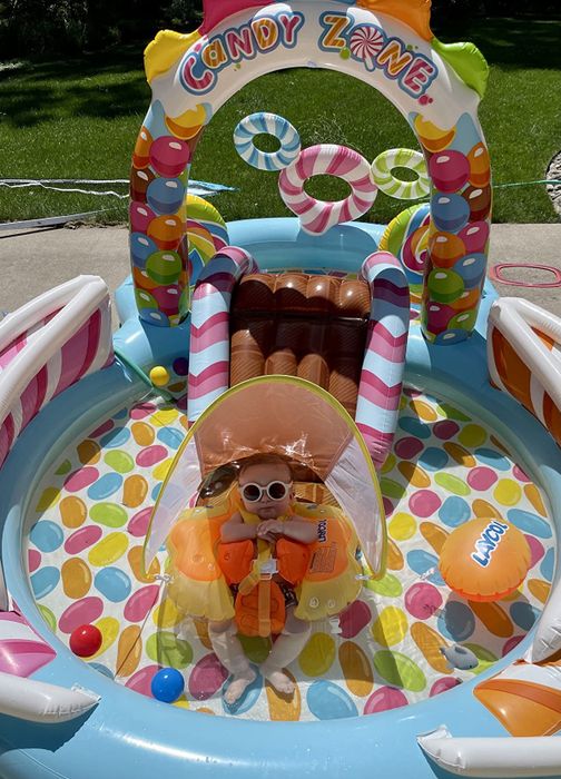 A young child sits inside a colorful inflatable play area, with the label visible.